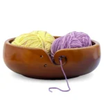 Wooden yarn bowl for crochet and amigurumi with yellow and purple yarn skeins and a swirl cutout for smooth yarn flow