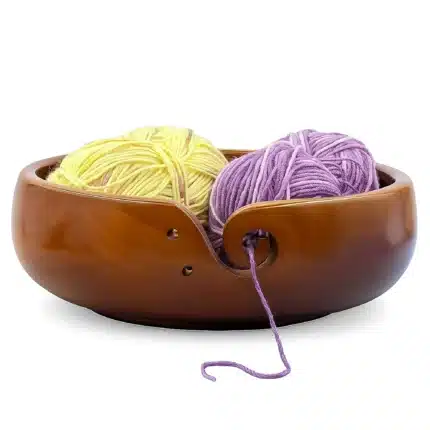 Wooden yarn bowl for crochet and amigurumi with yellow and purple yarn skeins and a swirl cutout for smooth yarn flow
