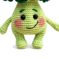 Close-up of the crochet broccoli pattern amigurumi showing face, blushed cheeks, horizontal body stitches and rounded legs
