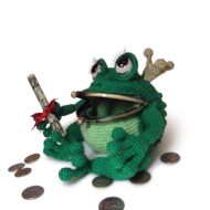 The crochet frog purse pattern seen at a three-quarter angle, showing the crown, the lashed eyes and the bobbled back