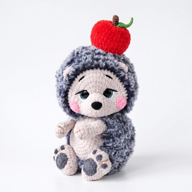 The finished crochet hedgehog pattern — a grey fluffy amigurumi hedgehog with a cream velvet face and a red crocheted apple balanced on his head