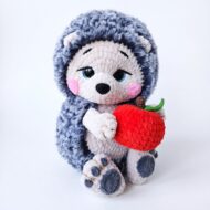 The crochet hedgehog pattern finished and holding its red crocheted apple