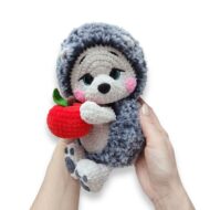 The crochet hedgehog pattern held in a pair of hands, showing how small the finished toy is