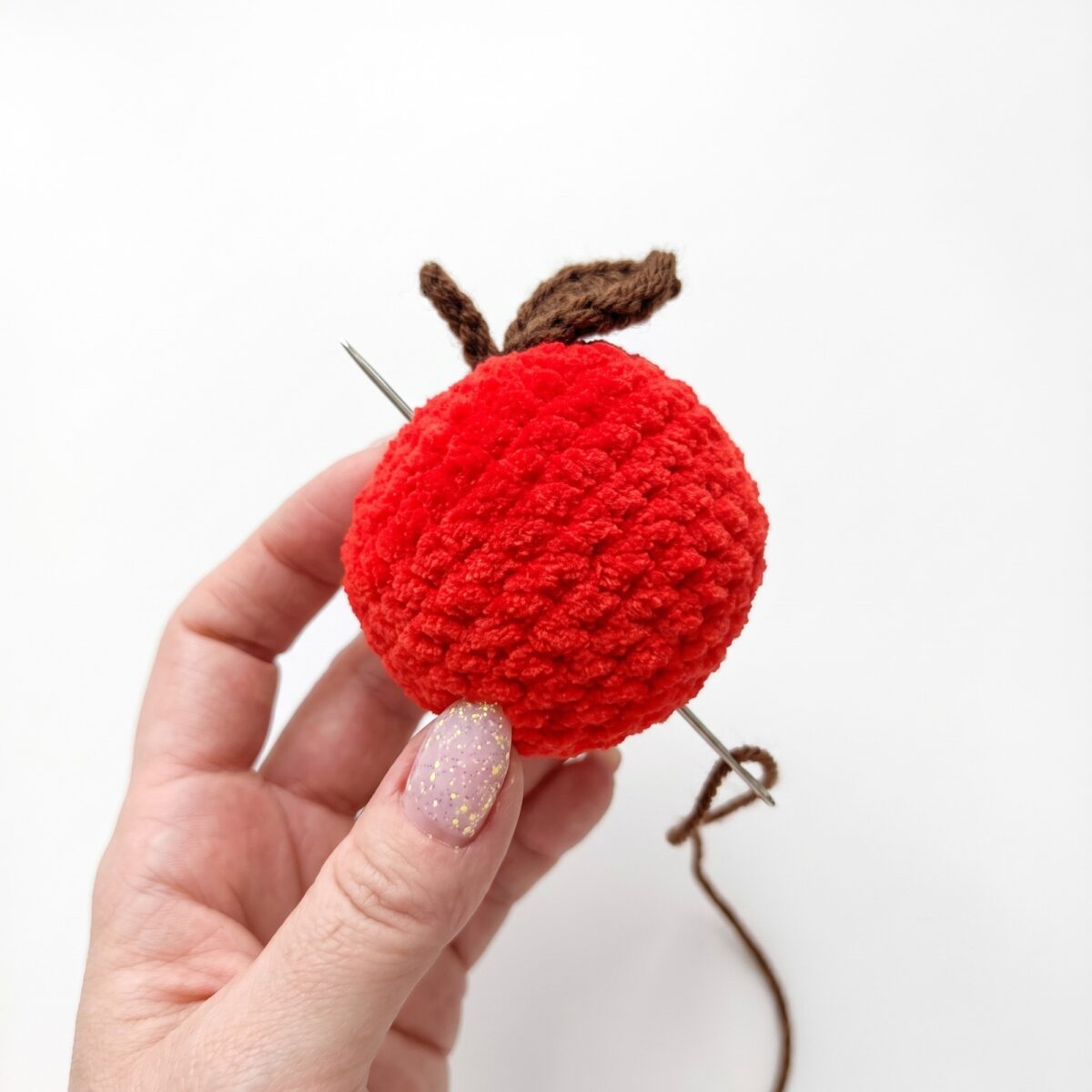 The apple from the crochet hedgehog pattern with its brown stem and green leaf