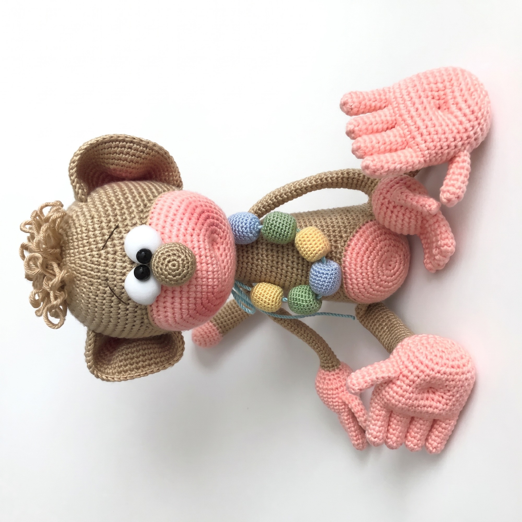 The finished crochet monkey pattern — a caramel amigurumi monkey with a pink muzzle, five separate fingers and a crocheted bead necklace