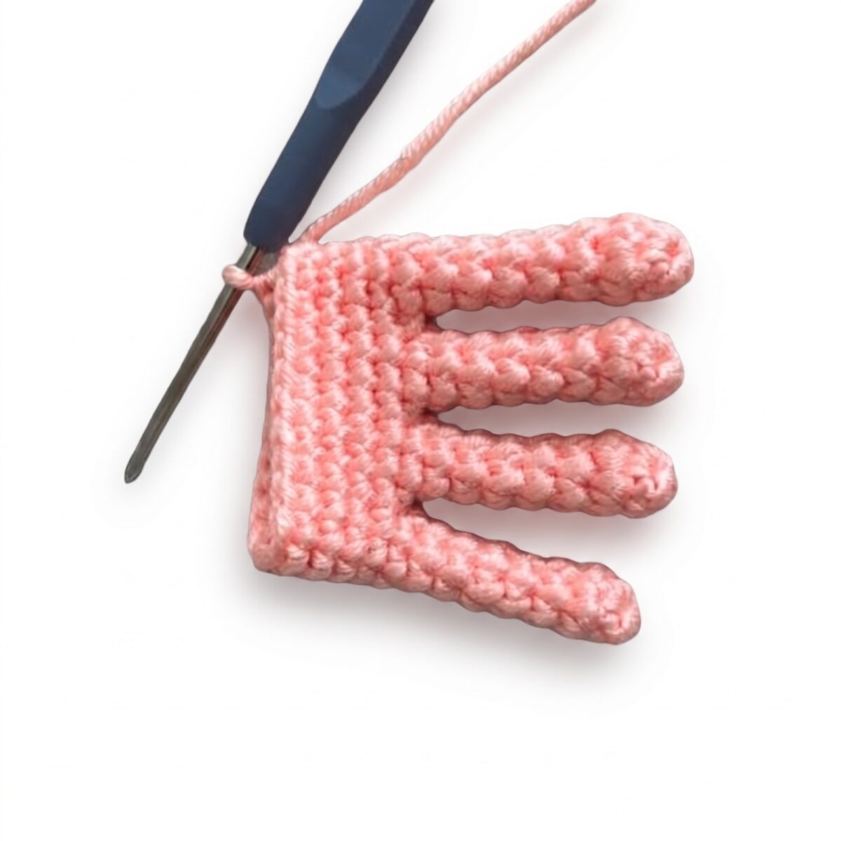 A pink crocheted hand with five separate fingers from the crochet monkey pattern